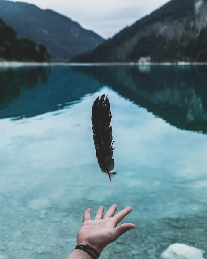 Feder schwebt über einer Hand vor einem Bergsee – Veränderung leicht gemacht und Fit for Flow
